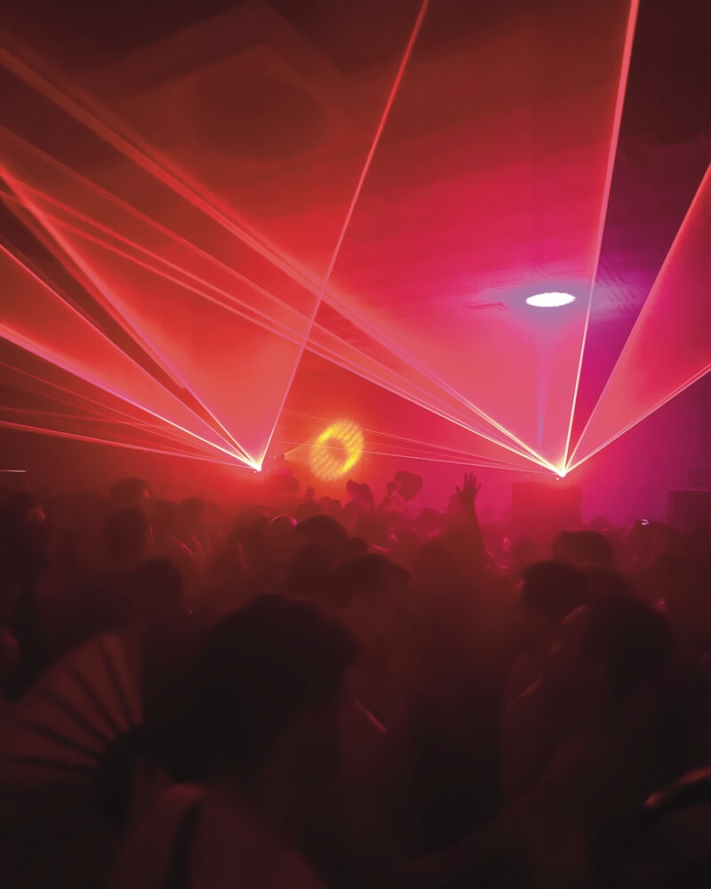 A photo from the party itself. Red lasers are shooting out and you can just about see the outline of a crowd. Everything is slightly blurry.