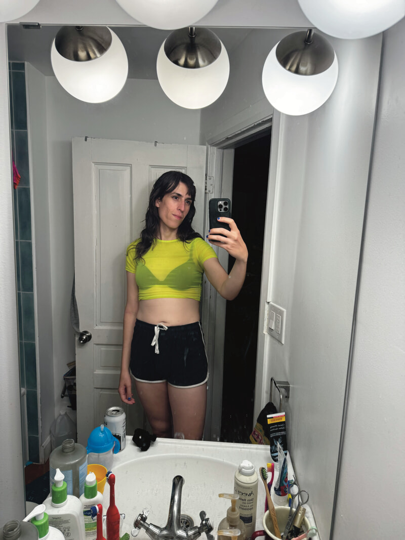 Bathroom mirror selfie. I'm wearing a cropped neon green mesh top over a black bra, and short gym shorts.
