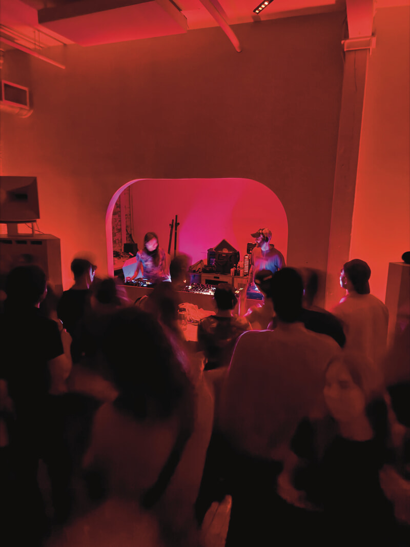 Two DJs in a booth stand amidst a crowd of dancers.